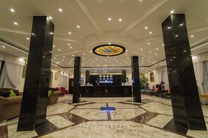 Un hall d’hôtel avec un comptoir d’accueil, des piliers en marbre noir et un sol à motifs.