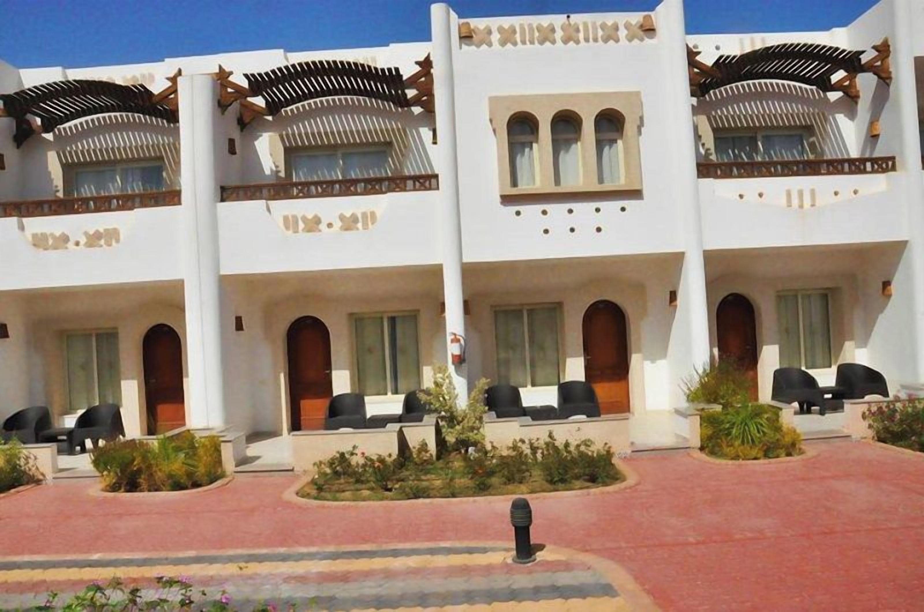A hotel with multiple balconies, outdoor seating, and a red-paved entrance.