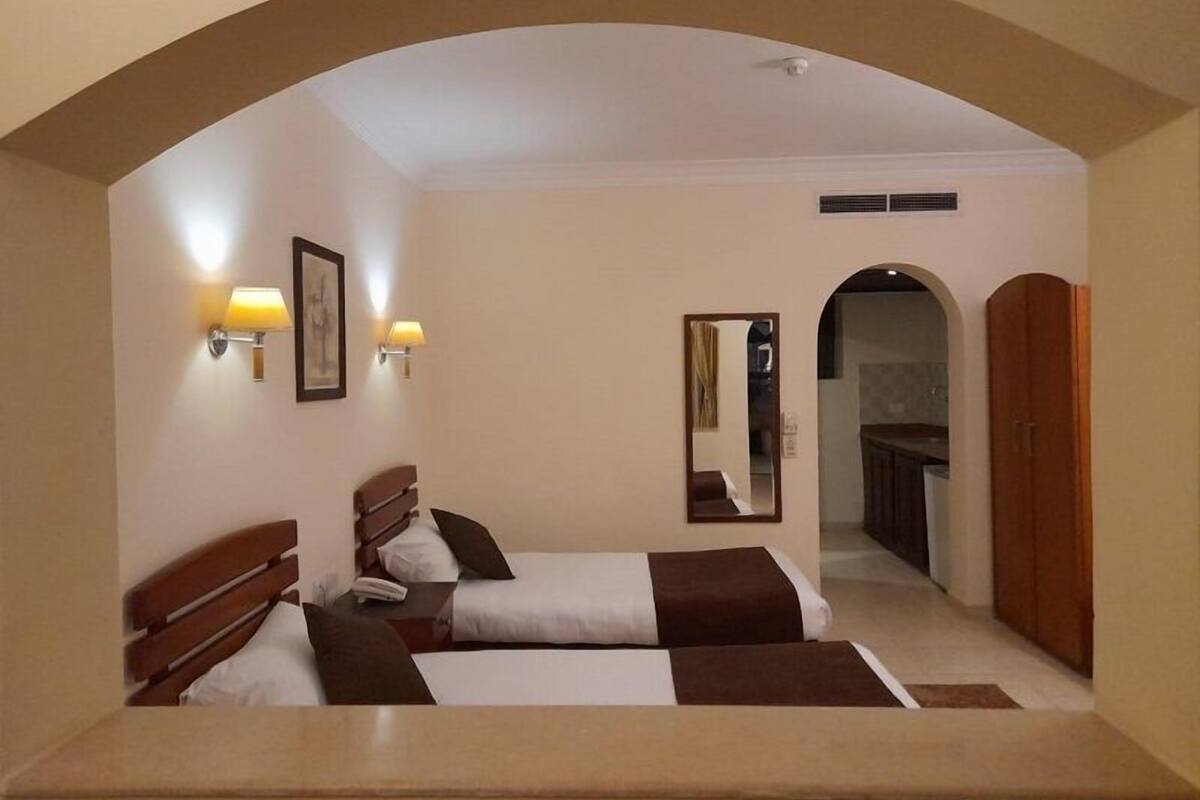 A hotel room with two beds, a mirror, wall-mounted lamps, and an arched doorway leading to a bathroom.