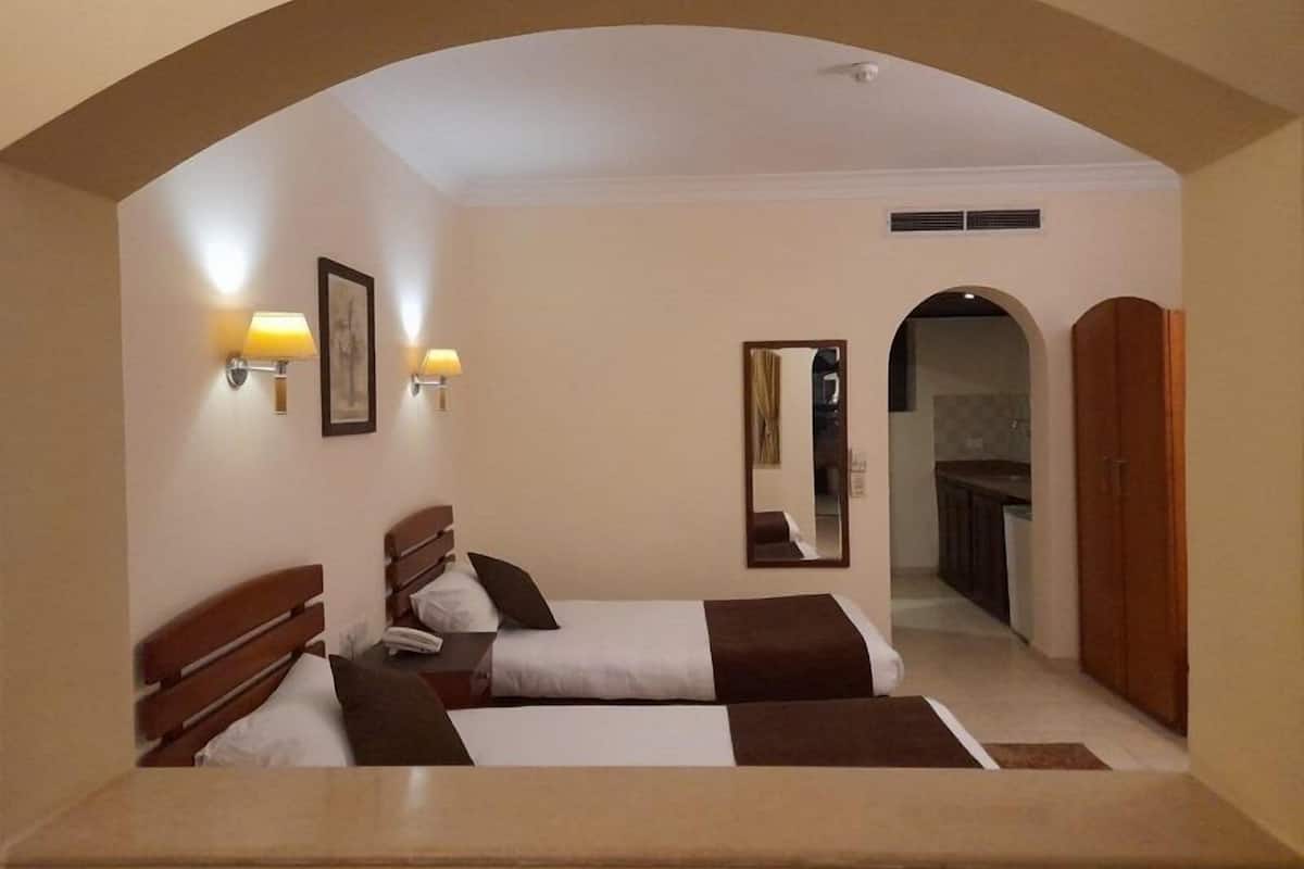 A hotel room with two beds, a mirror, wall-mounted lamps, and an arched doorway leading to a bathroom.