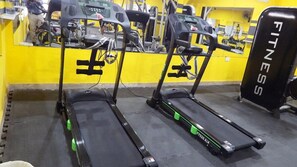 Une salle de sport équipée de tapis de course et d’un appareil de musculation noir portant l’inscription « FITNESS ».