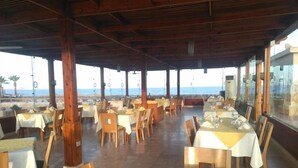 Ein Restaurant im Freien mit Tischen und Stühlen, das einen Blick auf einen Strand bietet.