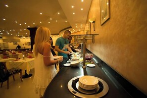 Un buffet avec plusieurs points de service, des invités qui dégustent les plats et une grande variété de mets présentés.