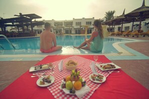 A poolside dining setup with a checkered tablecloth, plates of food, and a fruit bowl. - Tivoli Hotel Aqua Park (Sharm El Sheikh)