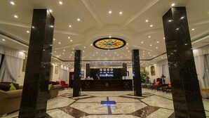 Eine Hotelhalle mit einer Rezeption, Marmorböden und einem großen Buntglasfenster.
