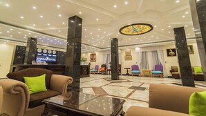 Eine Hotelhalle mit einer Rezeption, einer Sitzecke und einem großen Buntglasfenster.