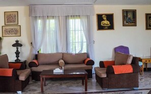 A living room with a sofa, two armchairs, a coffee table, and a lamp. There are two windows with curtains, a wall with framed artwork, and a statue. - Tivoli Hotel Aqua Park (Sharm El Sheikh)