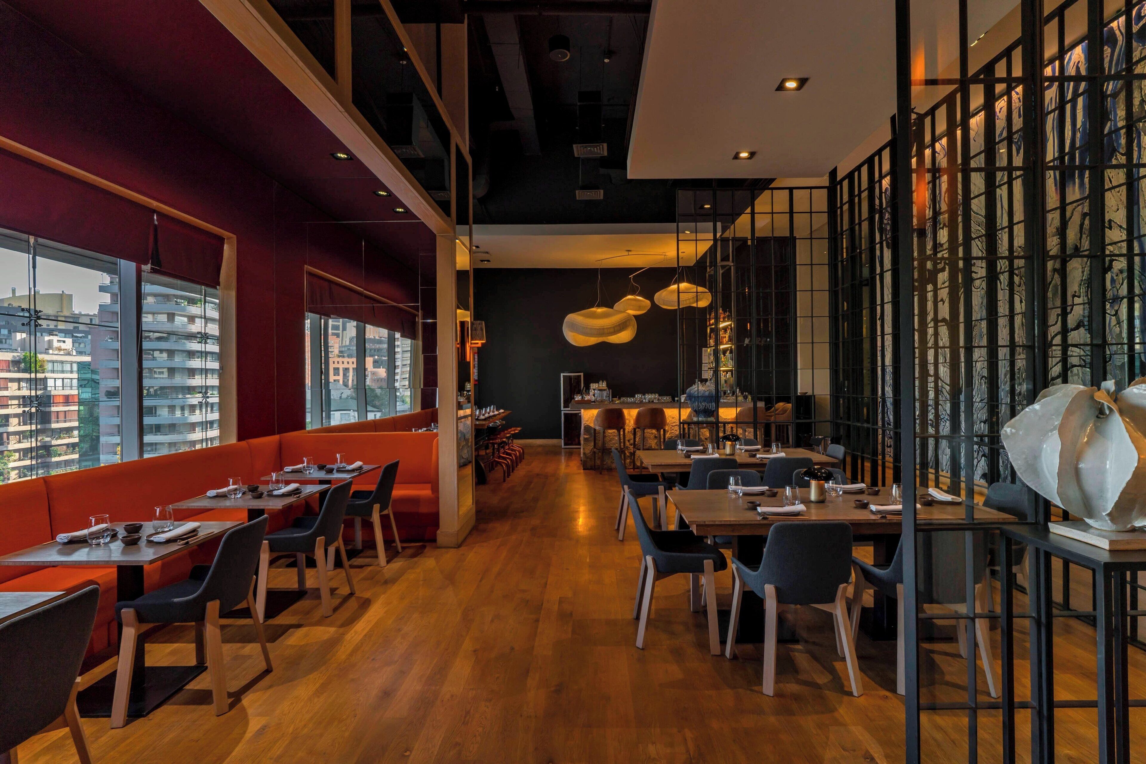 Een modern restaurant met hoge plafonds, houten vloeren en een gevarieerde zithoek, inclusief zitbanken en tafels.