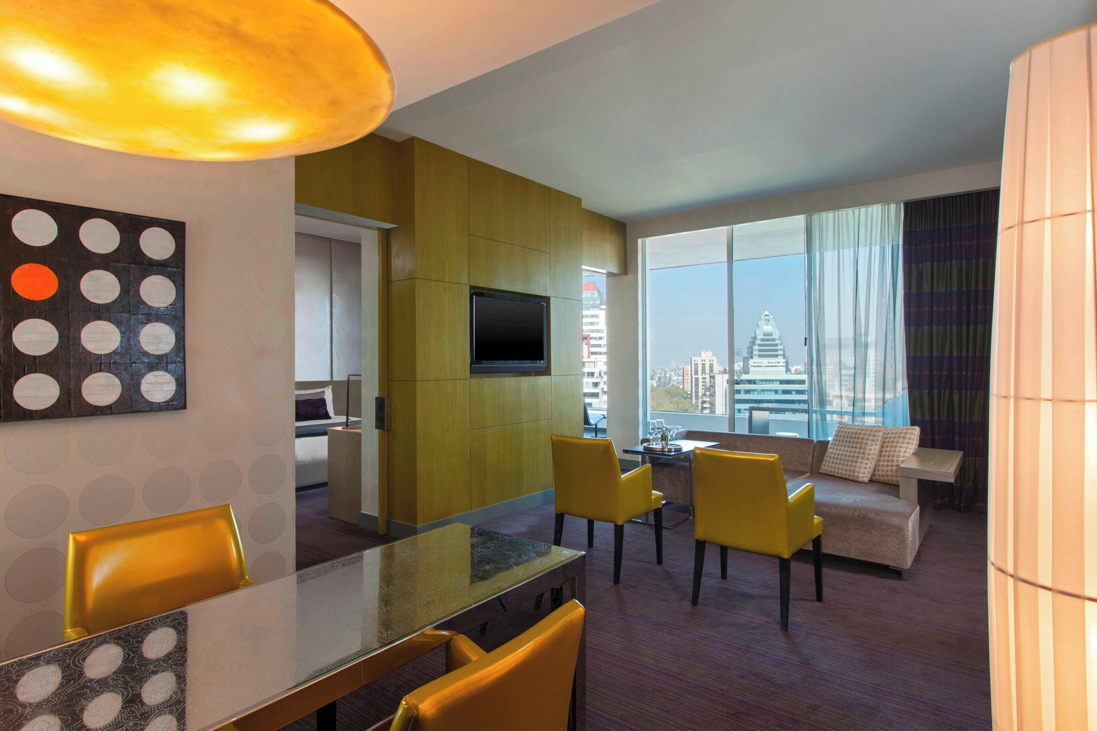 Une chambre d’hôtel moderne dotée d’un coin repas, d’un canapé et d’une grande fenêtre donnant sur la ville.