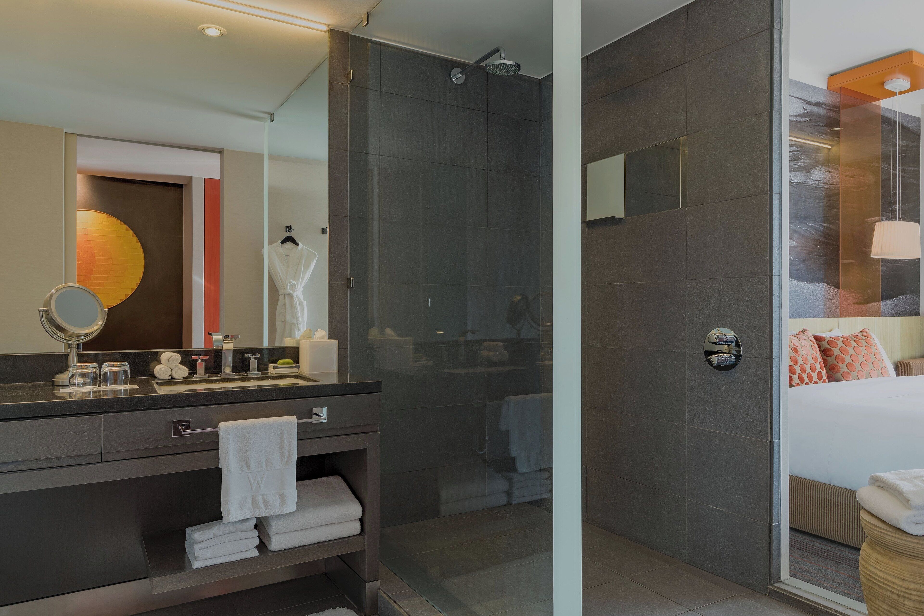 Un baño moderno con cabina de ducha de vidrio, tocador con espejo y cama con vistas.