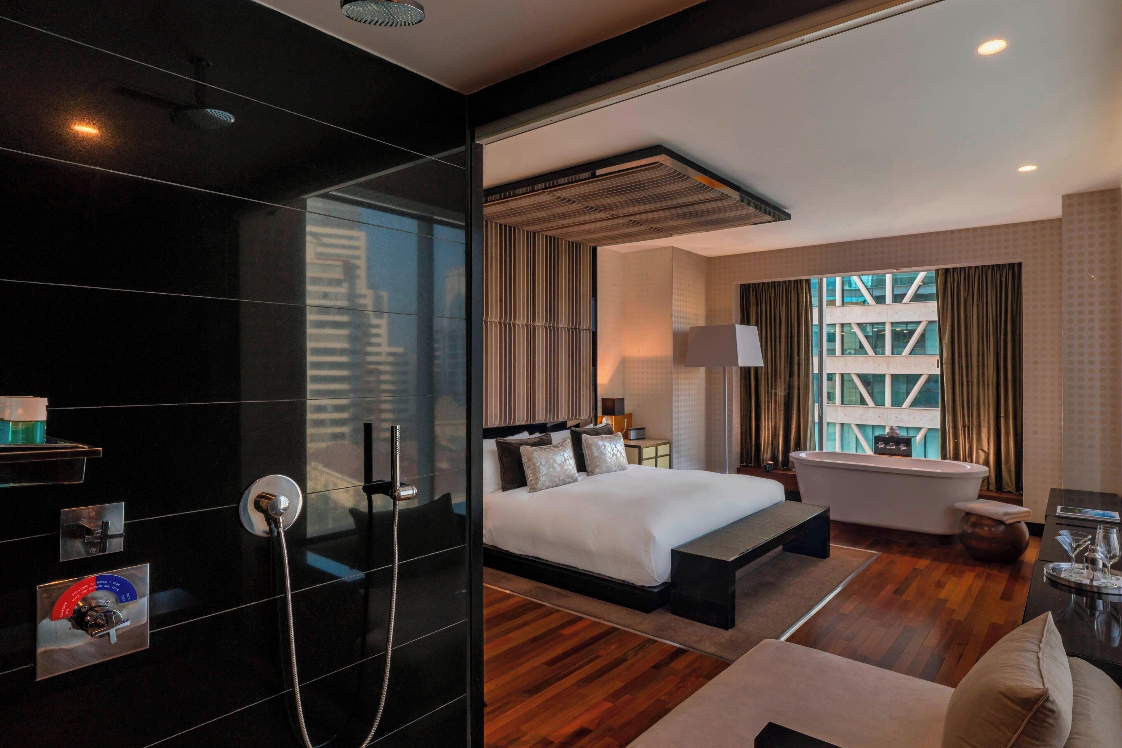 Een moderne hotelkamer met een groot bed, een aparte badkamer met bad en een uitzicht op de skyline door grote ramen.