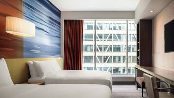 A hotel room with two beds, a desk, and a large window with a view of a building.