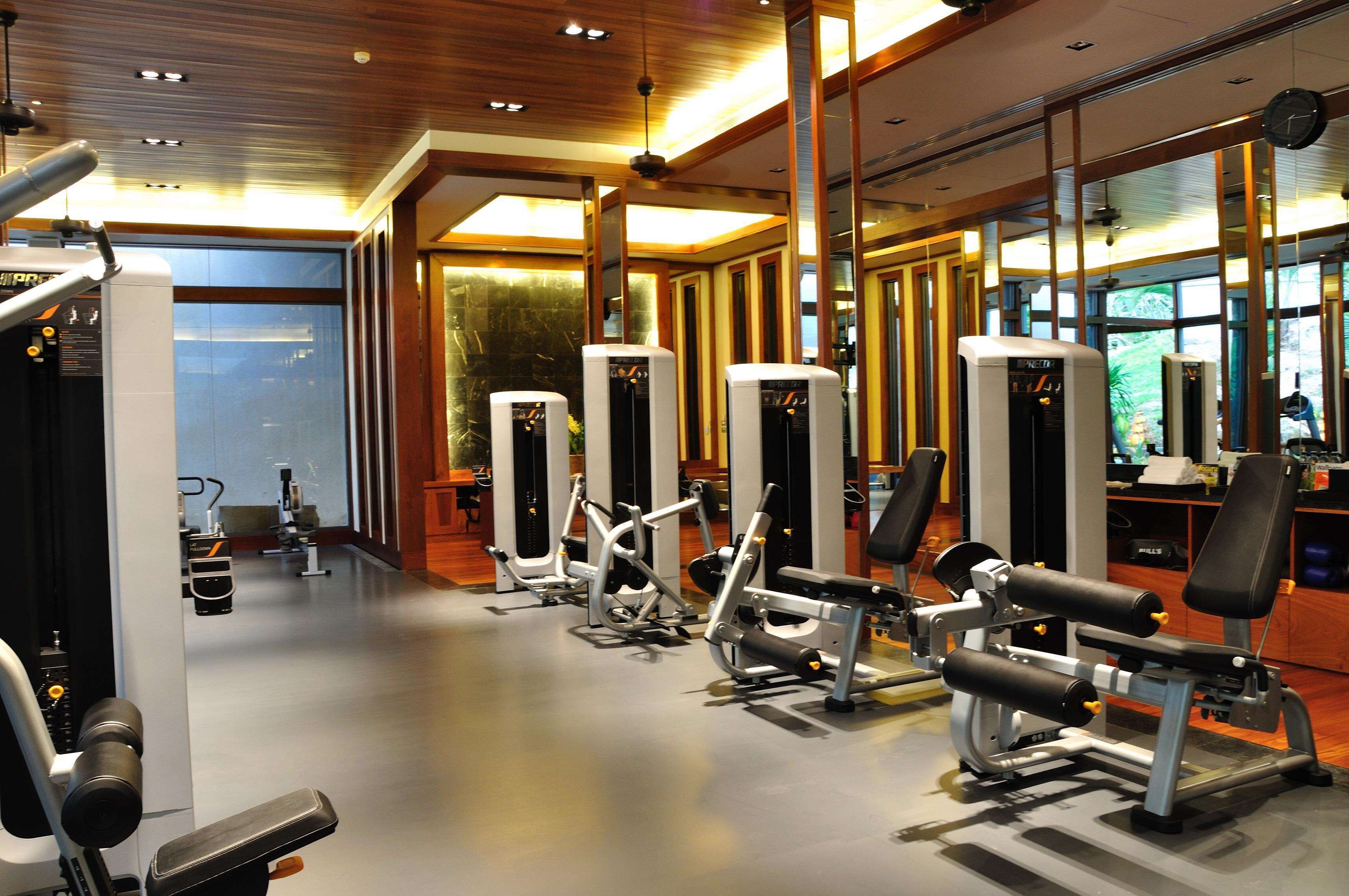A gym with various exercise machines, wooden flooring, and large windows.