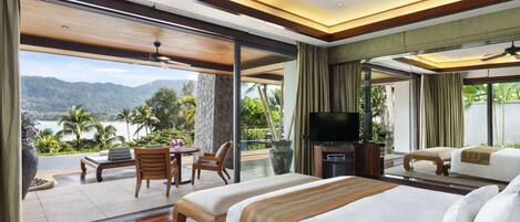 A hotel room with a large bed, a TV, and a balcony with a view of the mountains and water.