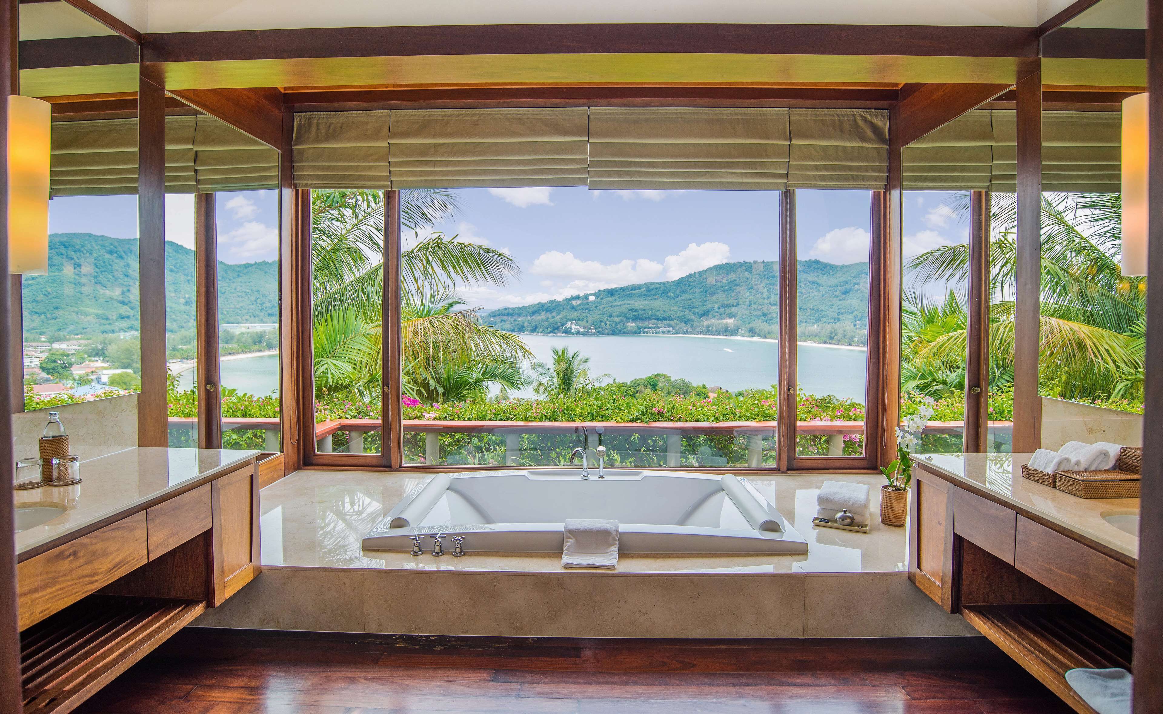 A spacious bathroom with a large bathtub, wooden vanity, and a view of a lake and mountains.