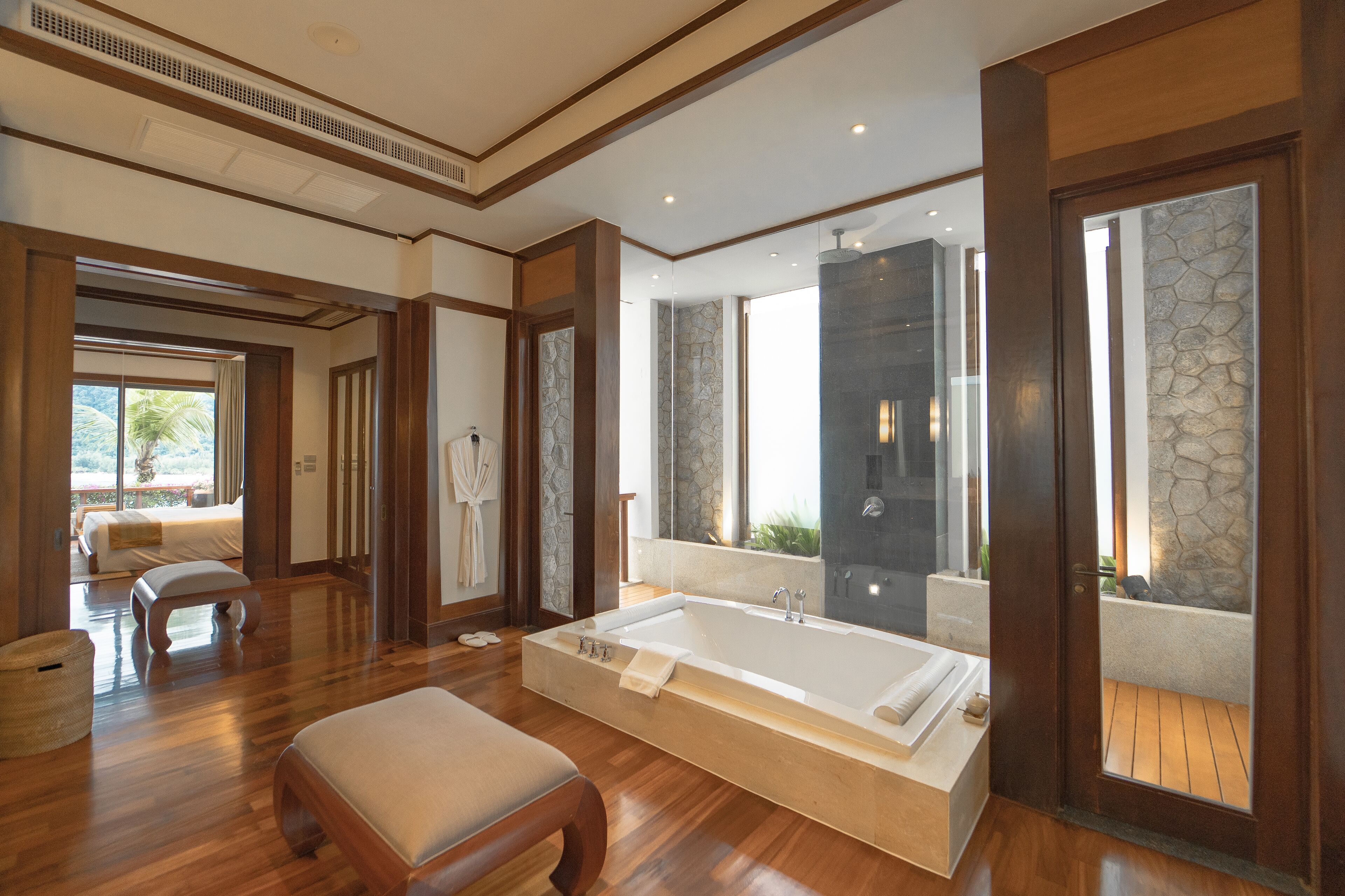 A spacious bathroom with a large bathtub, wooden flooring, and a view of the outdoors.