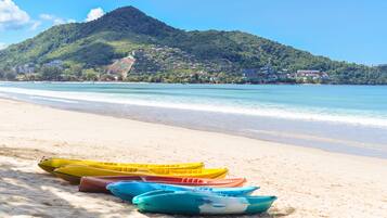 Una playa con kayaks alineados y una montaña al fondo.