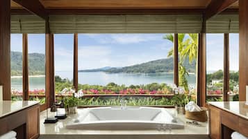 Une salle de bain dotée d’une grande baignoire, de meubles en bois et offrant une vue sur un lac et des montagnes.