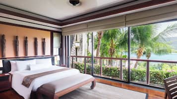 Un dormitorio amplio con una cama grande, un banco de madera y un balcón con vistas a palmeras y una masa de agua.