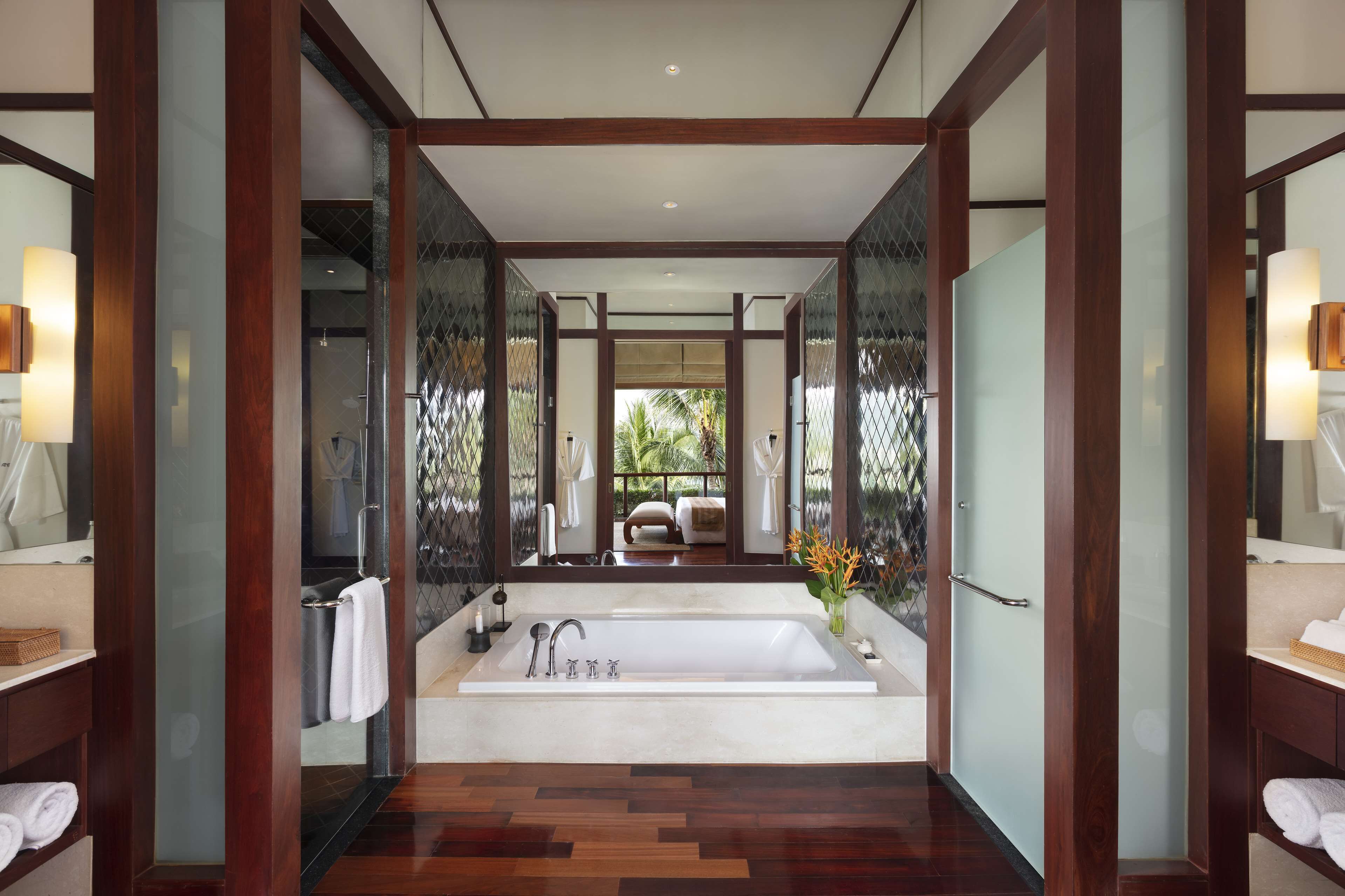 A modern bathroom with a large bathtub, wooden flooring, and glass partitions.