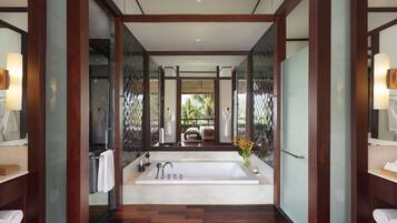 A modern bathroom with a large bathtub, wooden flooring, and glass partitions.