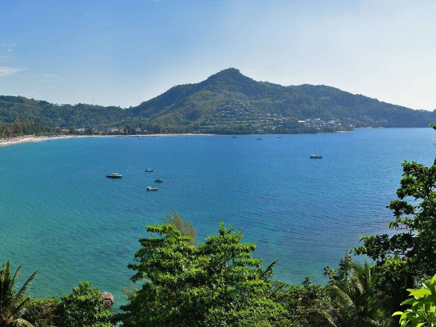 Vista costera con playa, barcos y montañas.