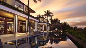 A luxurious resort with a large infinity pool, outdoor seating, and a well-lit entrance.