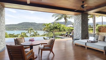 A wooden deck with a table and chairs, a sofa, and a view of a body of water and mountains.