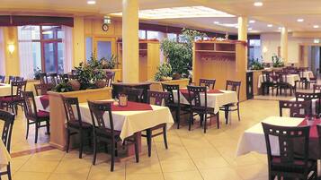 A restaurant with multiple tables and chairs, large windows, and potted plants.