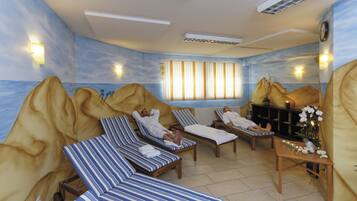 A spa room with reclining chairs, a massage table, and a view of the ocean through a window.