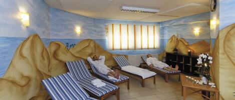 Ein Spa-Raum mit Liegestühlen, einer Massageliege und Meerblick durch ein Fenster.