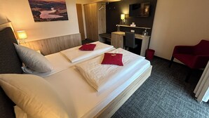 A hotel room with a large bed, a desk, a chair, and a painting on the wall.