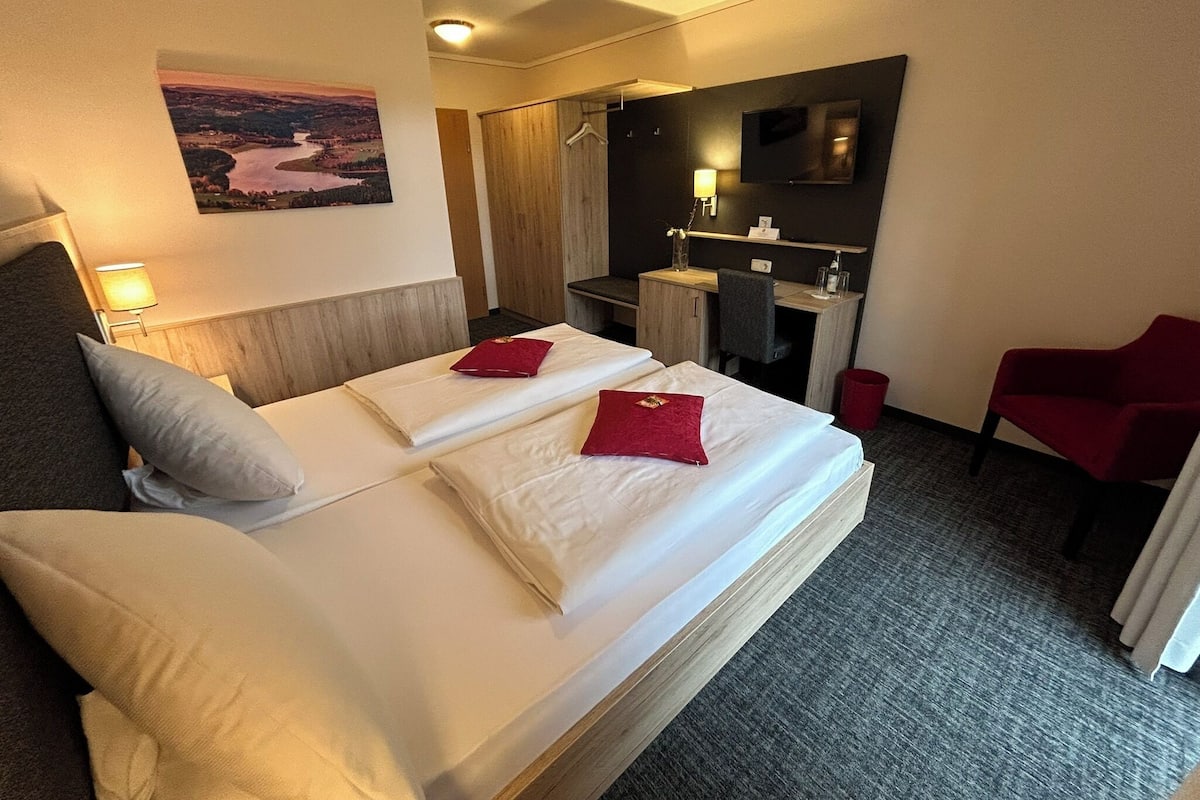 Una habitación de hotel con una cama grande, un escritorio, una silla y un cuadro en la pared.