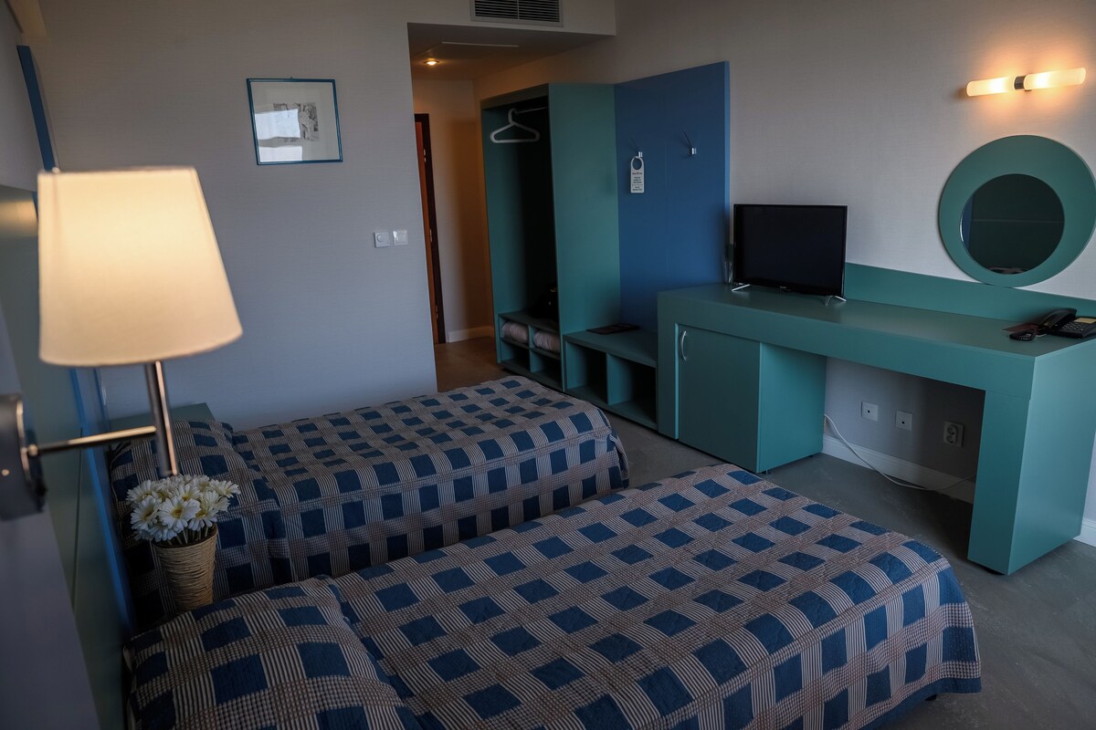 Une chambre avec deux lits, un bureau avec une télévision, une lampe et un miroir.