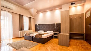 A modern hotel room with a large bed, a wooden wardrobe, a radiator, and a large window with curtains. - The Fontana Hotel (Novi Sad)