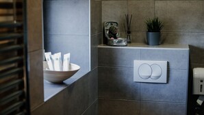 A bathroom with a towel rack, a bowl of toiletries, a potted plant, and a soap dispenser. - The Fontana Hotel (Novi Sad)