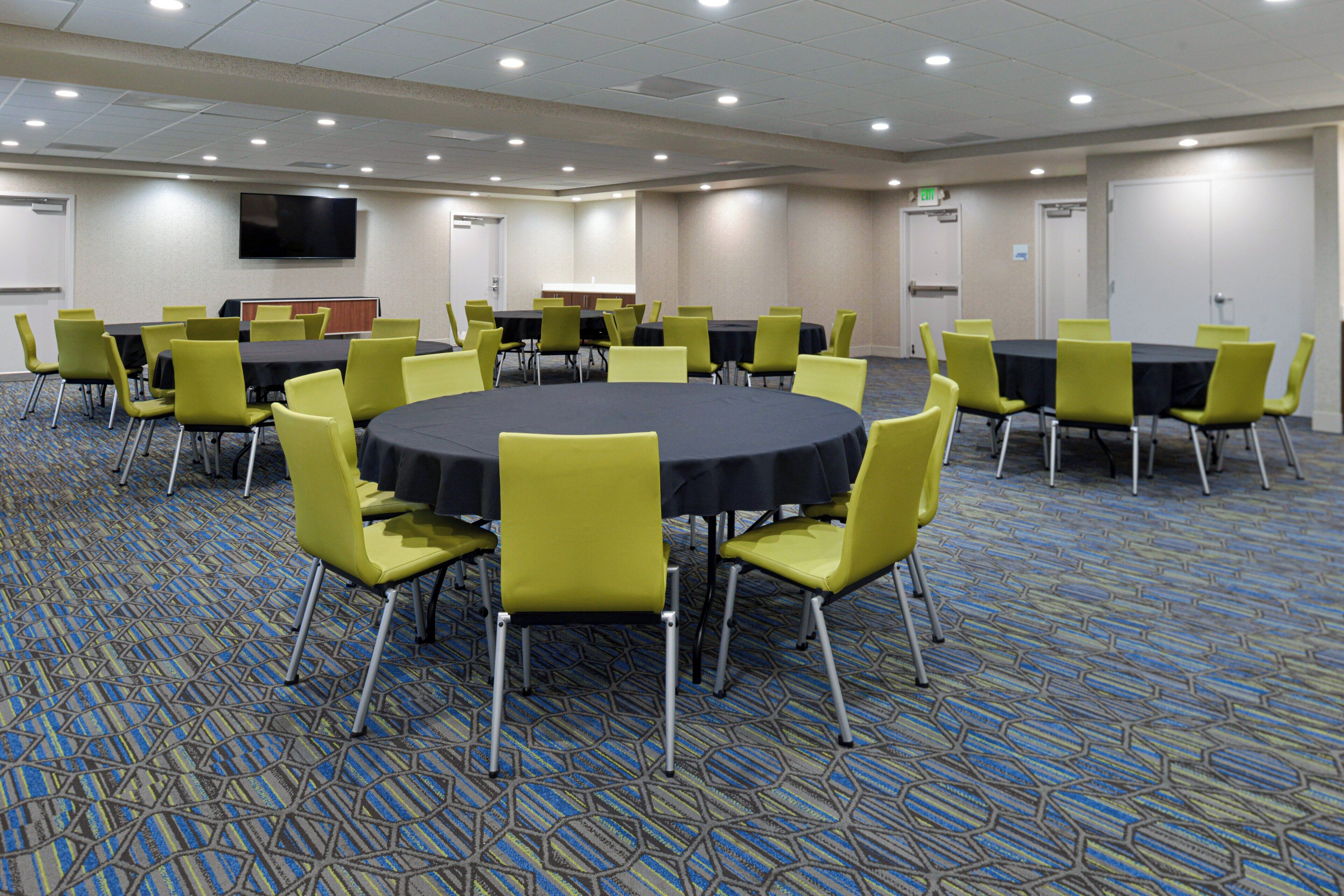 Une salle de conférence dotée de plusieurs tables et chaises, d’un sol recouvert de moquette et d’un téléviseur à écran plat fixé au mur.