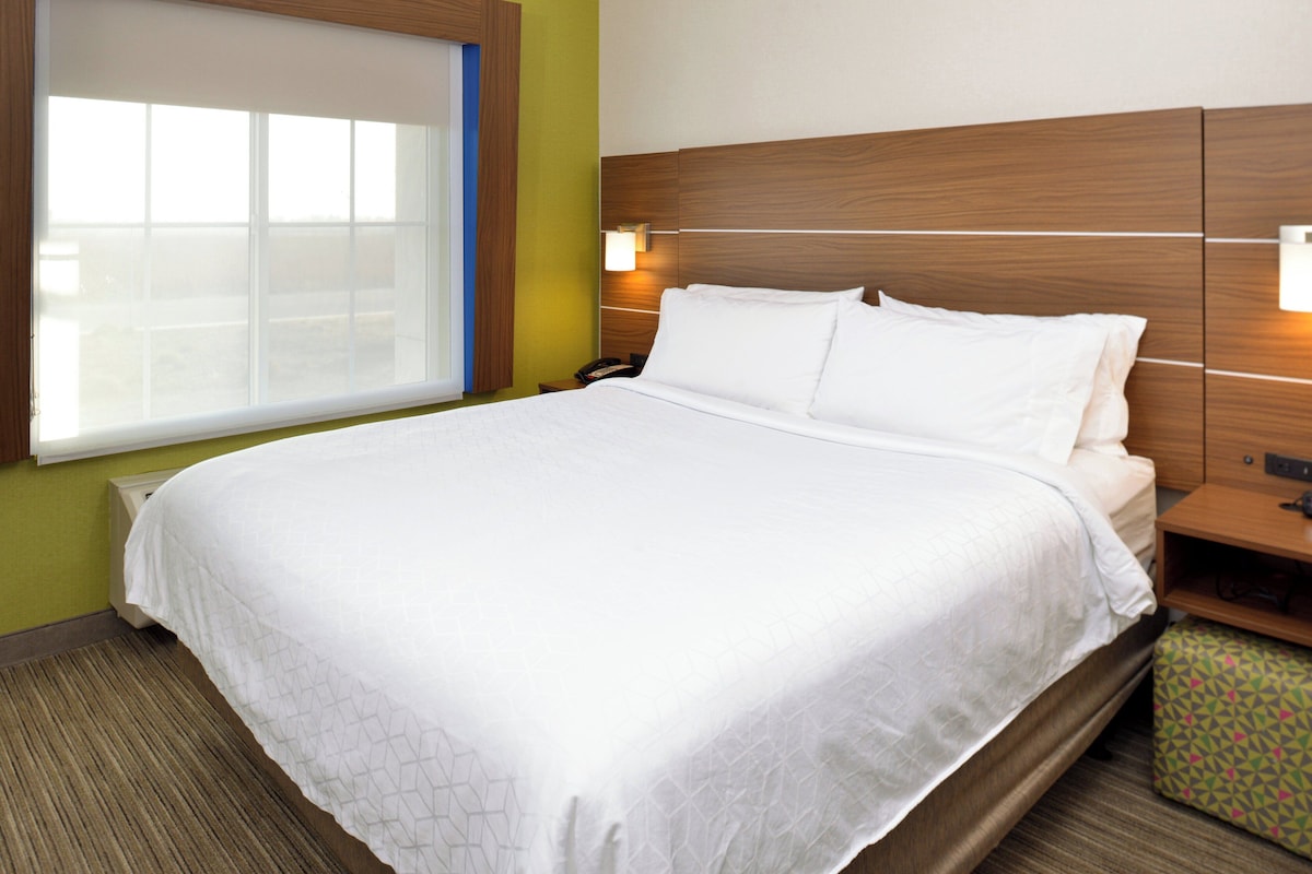 A hotel room with a large bed, a nightstand, a bedside lamp, and a window with blinds.