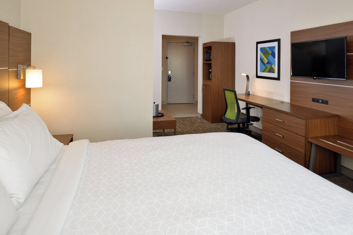 A hotel room with a bed, a desk, a chair, a television, and a door leading to another room.