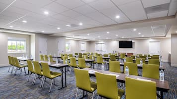Una sala de conferencias con sillas y mesas amarillas, y una pantalla grande.