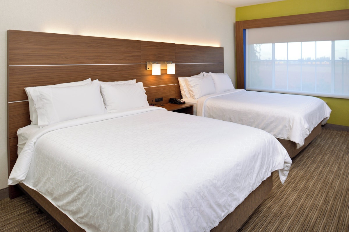 A hotel room with two beds, a wooden headboard, bedside lamps, and a window.