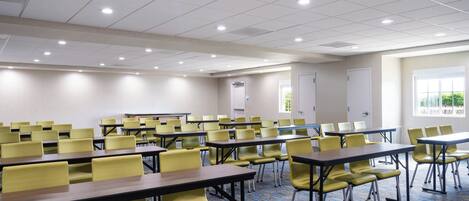A conference room with rows of yellow chairs and tables, a patterned carpet, and a ceiling with recessed lighting.