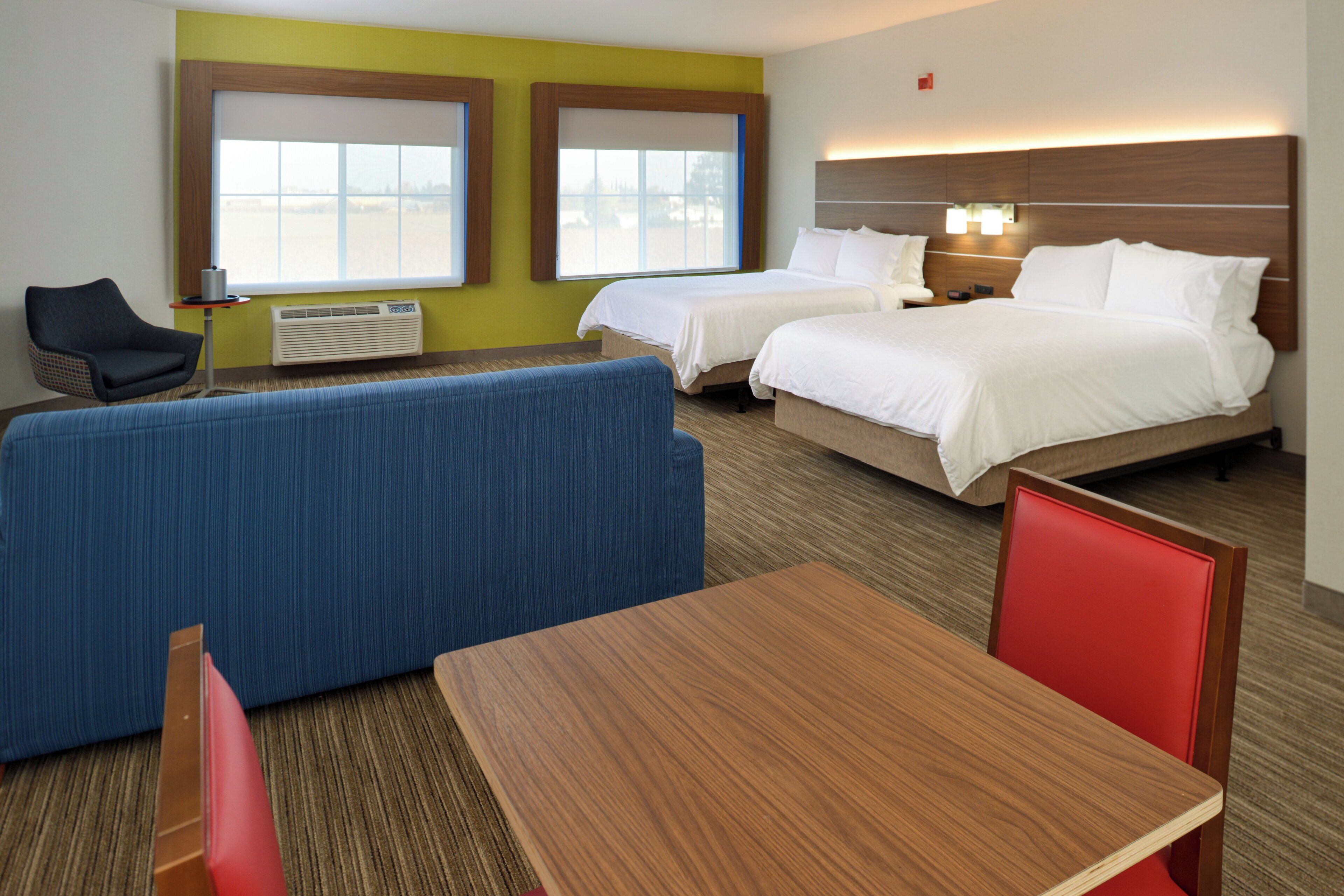 A hotel room with two beds, a sofa, a table, and a chair.