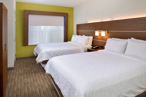 A hotel room with two beds, a window with blinds, a nightstand with a phone, and a wall-mounted light fixture.