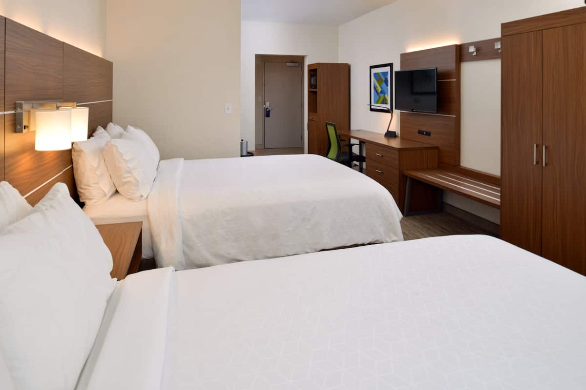 A hotel room with two beds, a desk, a chair, a TV, and a wardrobe.