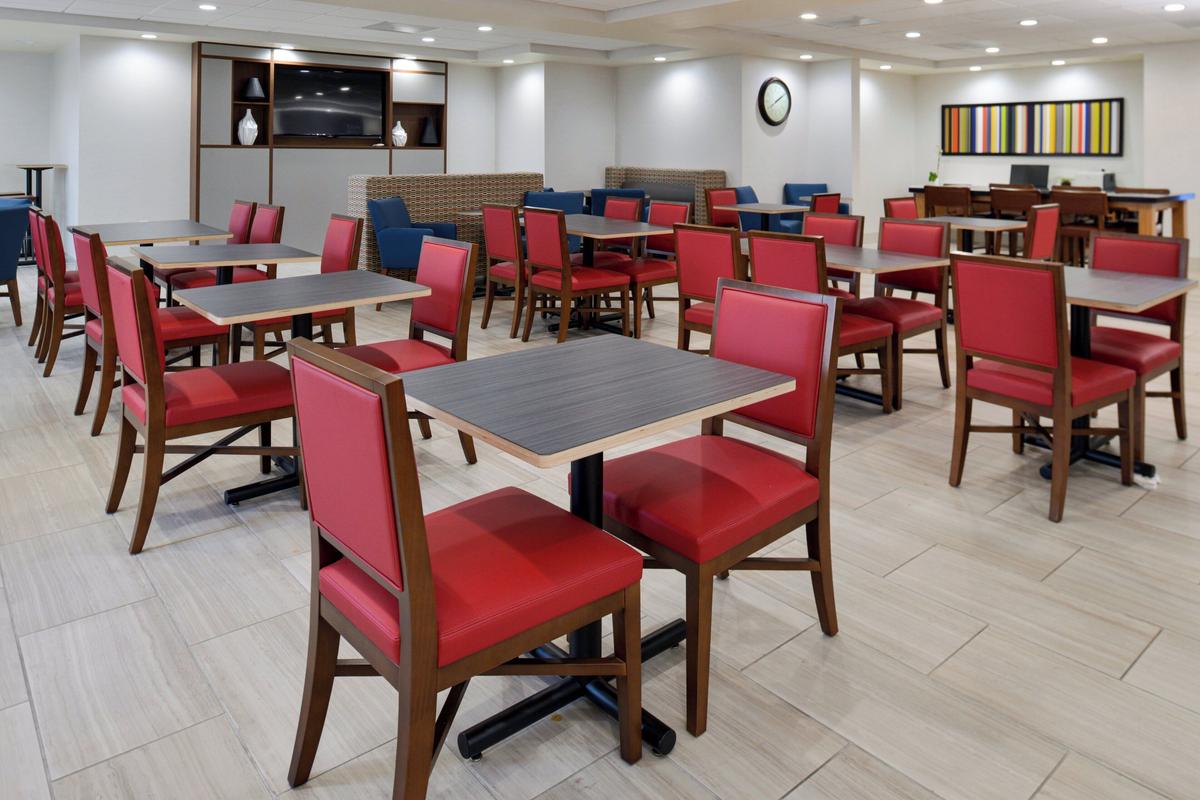 A dining area with multiple tables and chairs, a flat-screen TV mounted on the wall, and a clock.