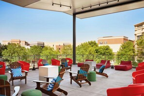 An outdoor seating area with various chairs and tables, a covered section with lights, and a view of buildings and trees. - Aloft by Marriott Leawood-Overland Park (Leawood)