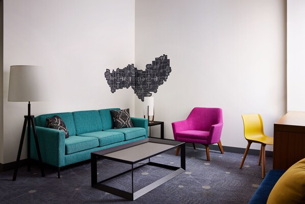 A modern living room with a teal sofa, a pink armchair, a yellow chair, a coffee table, and a floor lamp. - Aloft by Marriott Leawood-Overland Park (Leawood)