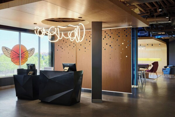 A modern reception desk with a nameplate, a decorative butterfly on the window, and a unique ceiling light design. - Aloft by Marriott Leawood-Overland Park (Leawood)