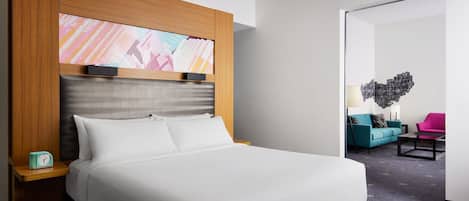 A hotel room with a large bed, a wooden headboard, a nightstand with a clock, and a wall art piece.